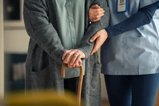 Care worker supporting elderly woman with walking stick